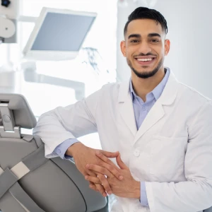 Cosmetic dentist in Garden City smiling in a modern dental clinic, standing beside advanced dental equipment and ready to provide professional smile makeover treatments